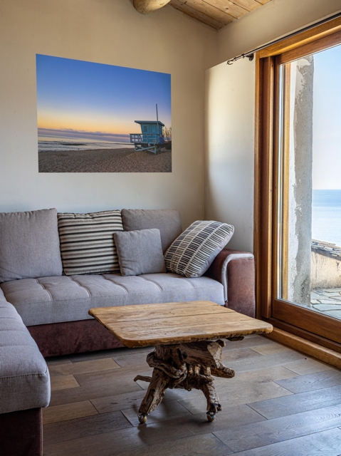 Living room with a large window, gray sofa, wooden coffee table and a canvas print of a California lifeguard tower at sunrise.