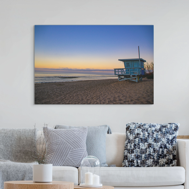 Canvas print of a California lifeguard tower at sunrise on a wall above a sofa with decorative pillows.