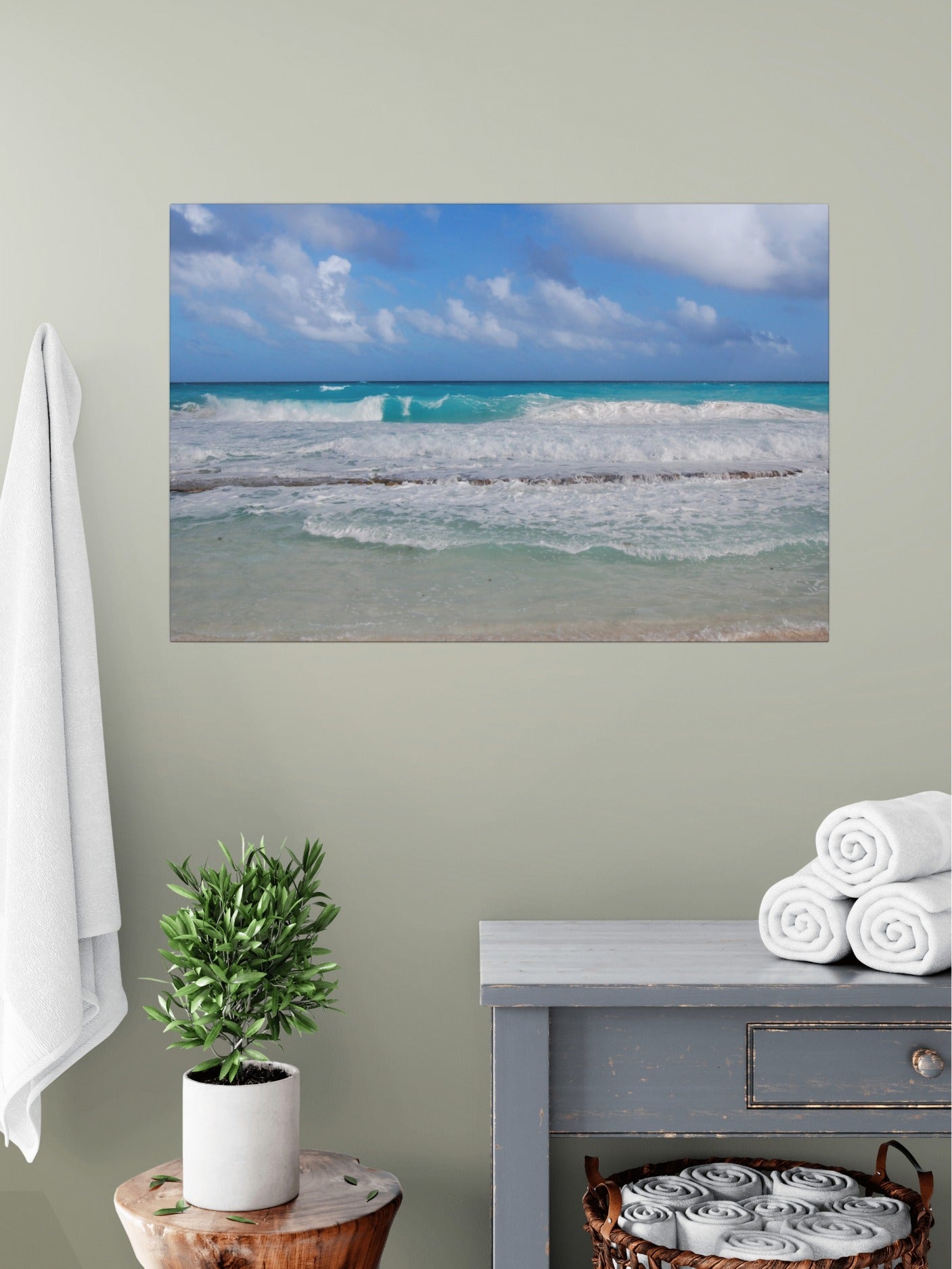 Cancun Caribbean turquoise waves breaking on sand canvas print on a wall above a table with a plant and folded towels.
