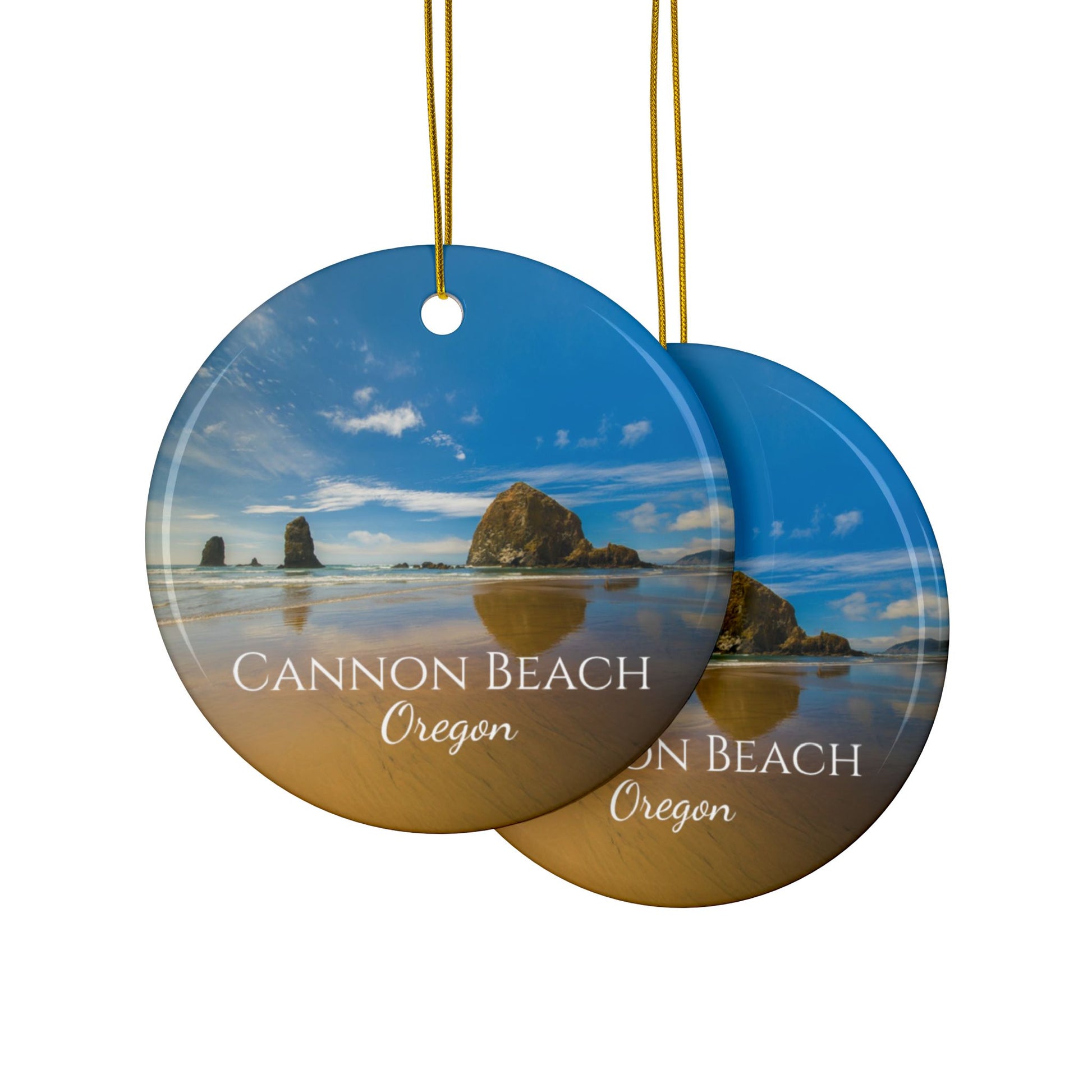 Front and back side of a ceramic holiday ornament featuring a photograph of Haystack Rock at Cannon Beach, Oregon, with blue sky reflections on the shoreline