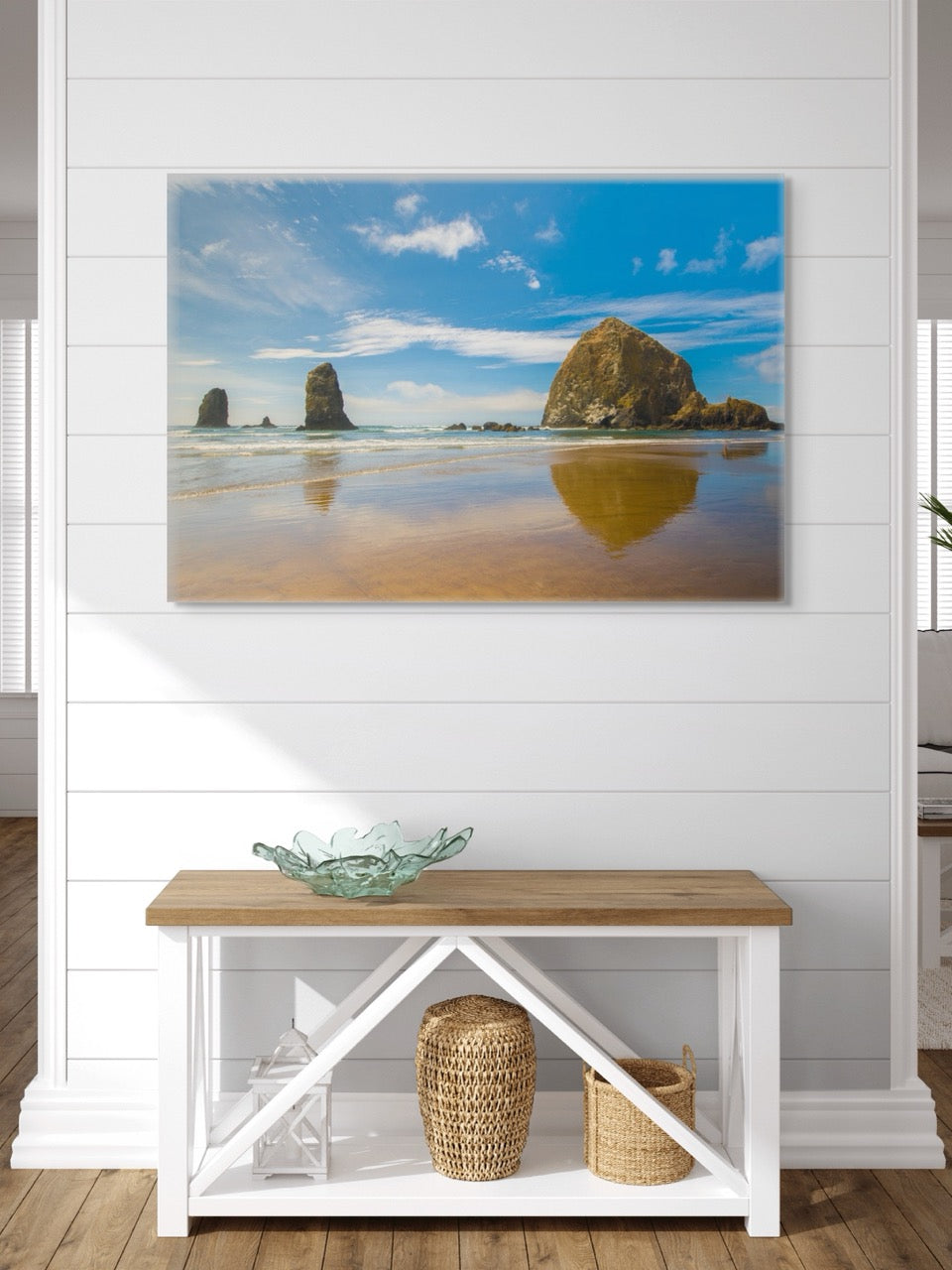 Large canvas print featuring a view of Haystack Rock and other rock off the coast of Cannon Beach, Oregon on a wall above a wooden bench with storage shelves.