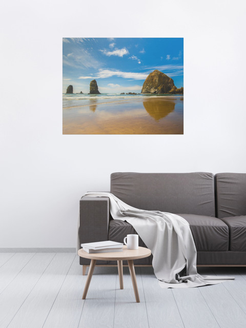 Living room with a gray sofa, round wooden coffee table, and a large canvas print featuring a view of Haystack Rock and other rock off the coast of Cannon Beach, Oregon on the wall.