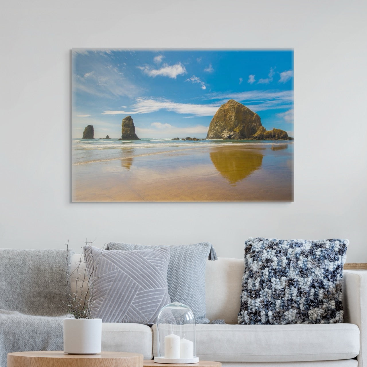 A canvas print featuring a view of Haystack Rock and other rock off the coast of Cannon Beach, Oregon above a living room sofa with decorative pillows.
