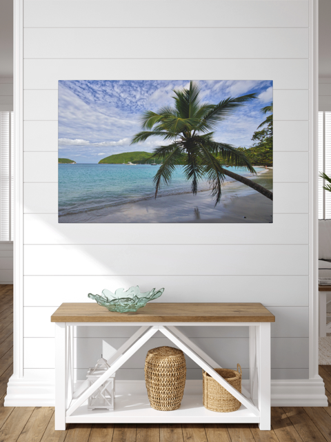 A canvas print of a tropical beach scene on a white wall above a wooden bench.