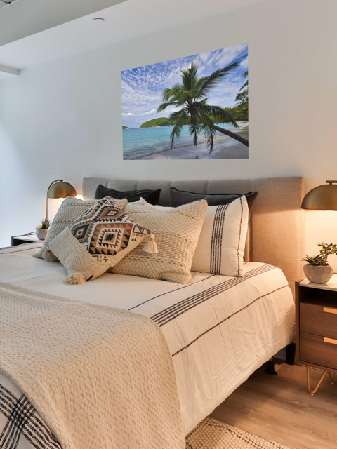 Bedroom with a bed featuring decorative pillows and a canvas print of a tropical beach scene on the wall.