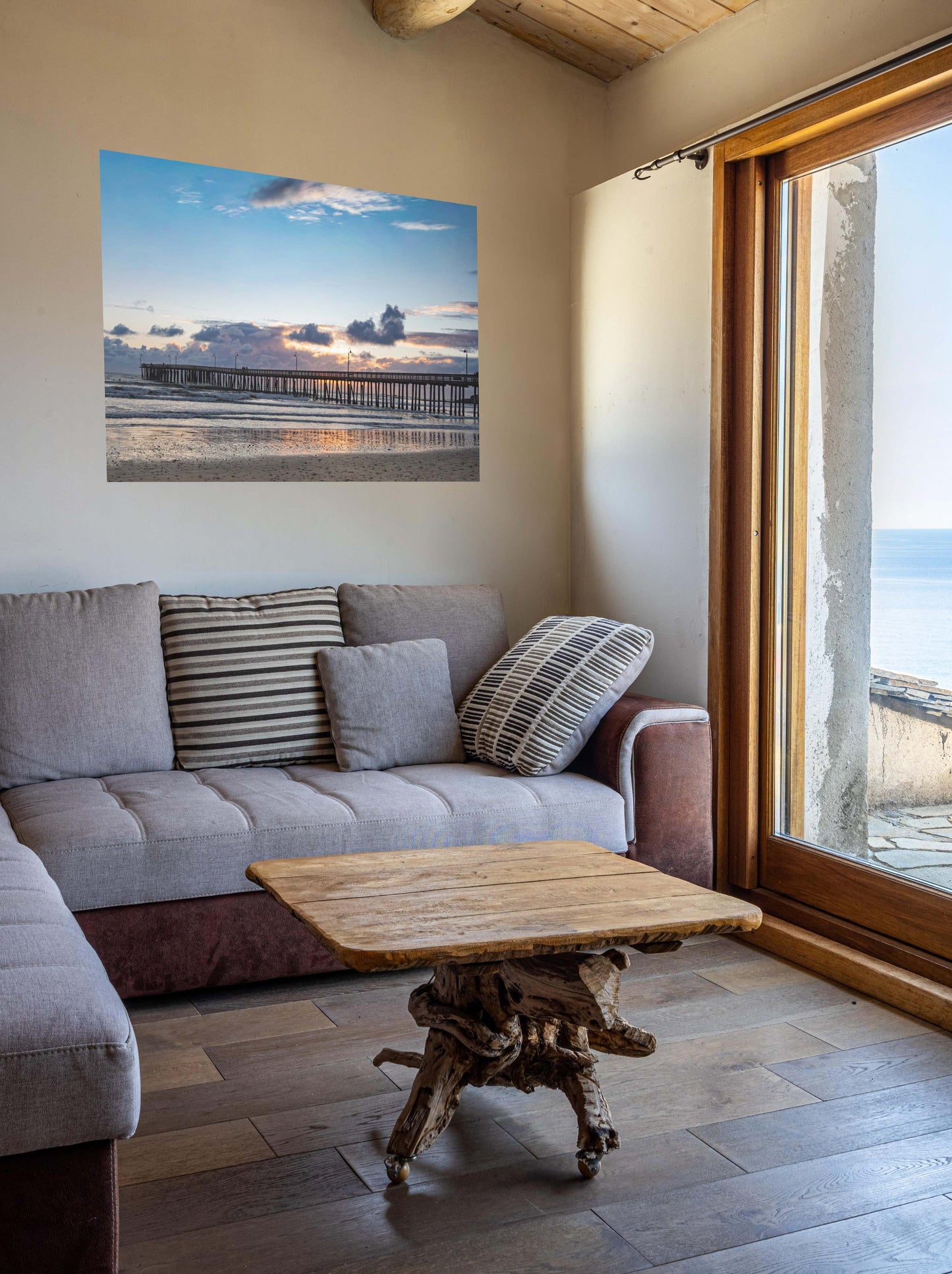 Living room with a gray sofa, wooden coffee table, and a Cayucos Pier sunset canvas print.