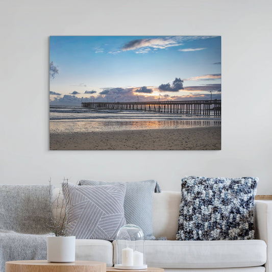 Cayucos Pier sunset canvas print on a wall above a sofa with decorative pillows.