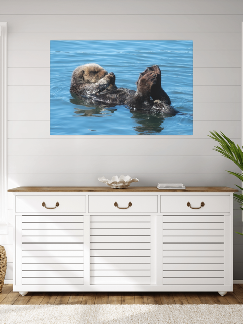 A sea otter swimming in water on a wall art above a white cabinet with wooden top.