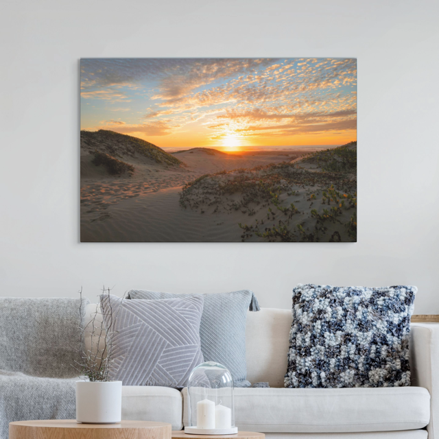 Canvas print of a beach dunes sunset hanging above a sofa with decorative pillows.