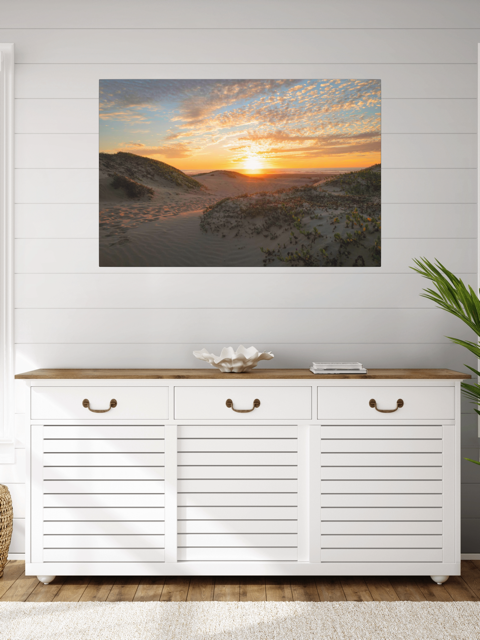 White cabinet with wooden top below a canvas print of a beach dunes sunset on a white wall.