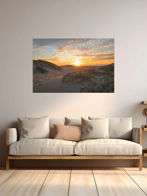 A canvas print of a beach dunes sunset on the wall over a beige sofa.