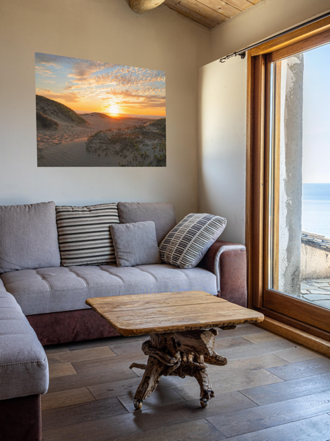 Living room with a gray sofa, wooden coffee table, and a sunset over a beach scene on the wall.