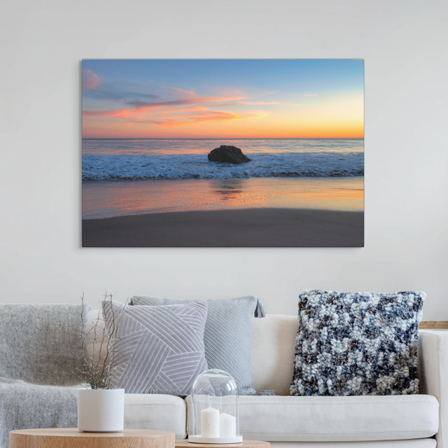 Beach sunset canvas print on a wall above a sofa with decorative pillows.