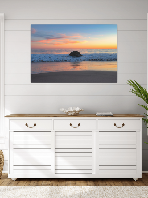 White cabinet with wooden top against a wall with a canvas print of a colorful sunset behind an ocean rock