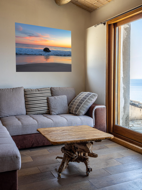 Living room with a gray sofa, wooden coffee table, and a canvas print of a colorful sunset behind an ocean rock on the wall.