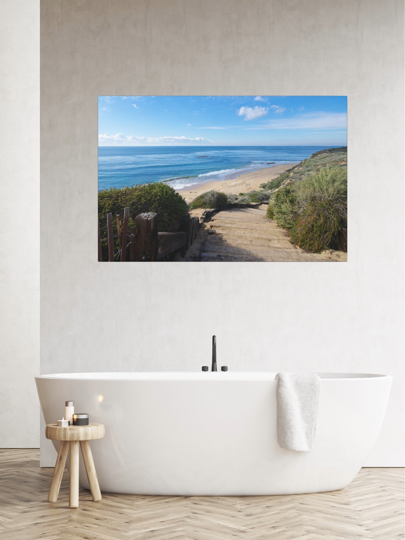 Bathroom with a canvas print of the wooden stairs leading to Crystal Cove State Beach in Orange County California, a freestanding bathtub, and a small wooden stool.