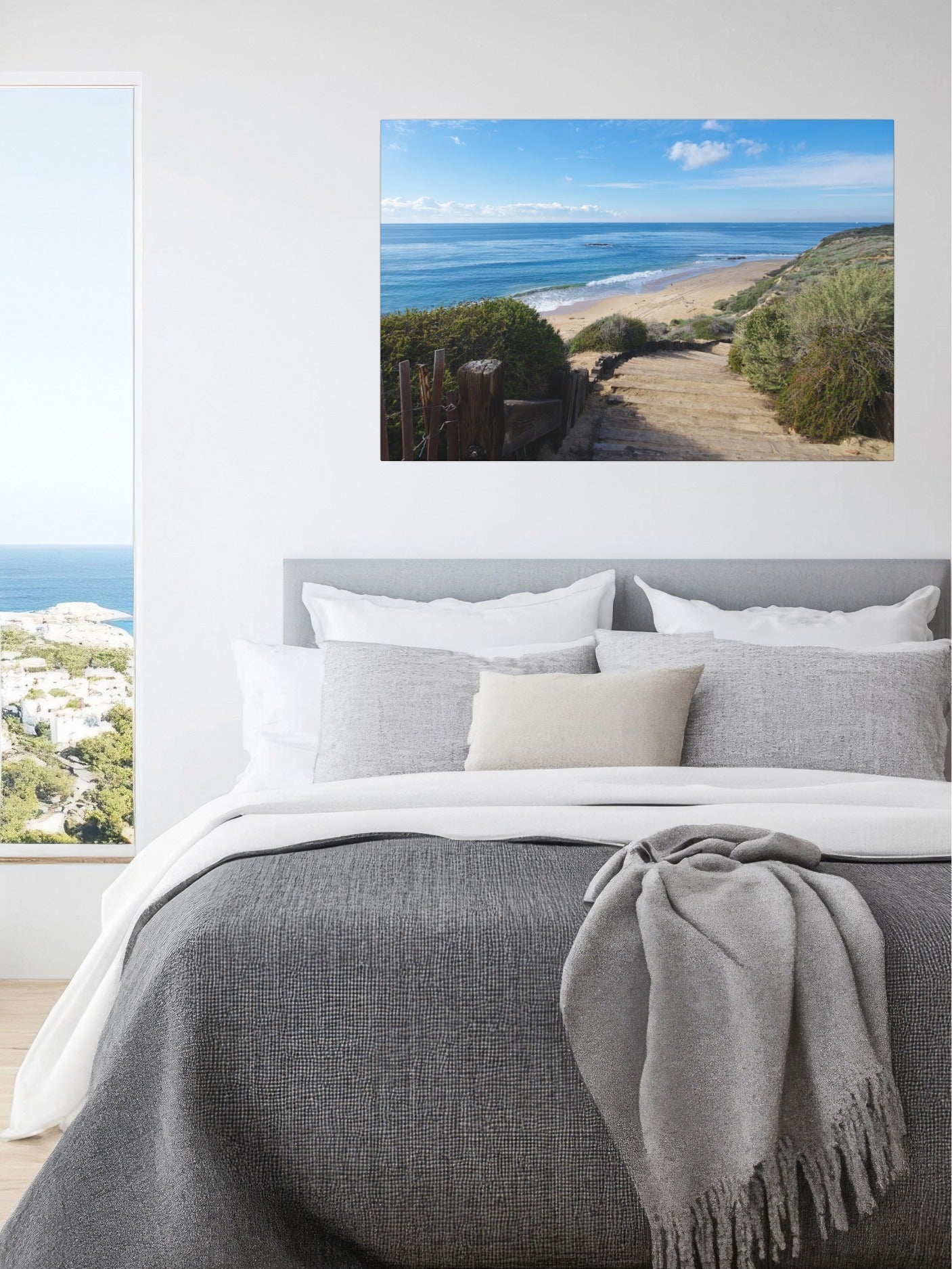 Bedroom with a large window showing a scenic view of a beach and ocean and a canvas print of the wooden stairs leading to Crystal Cove State Beach in Orange County California on the wall.