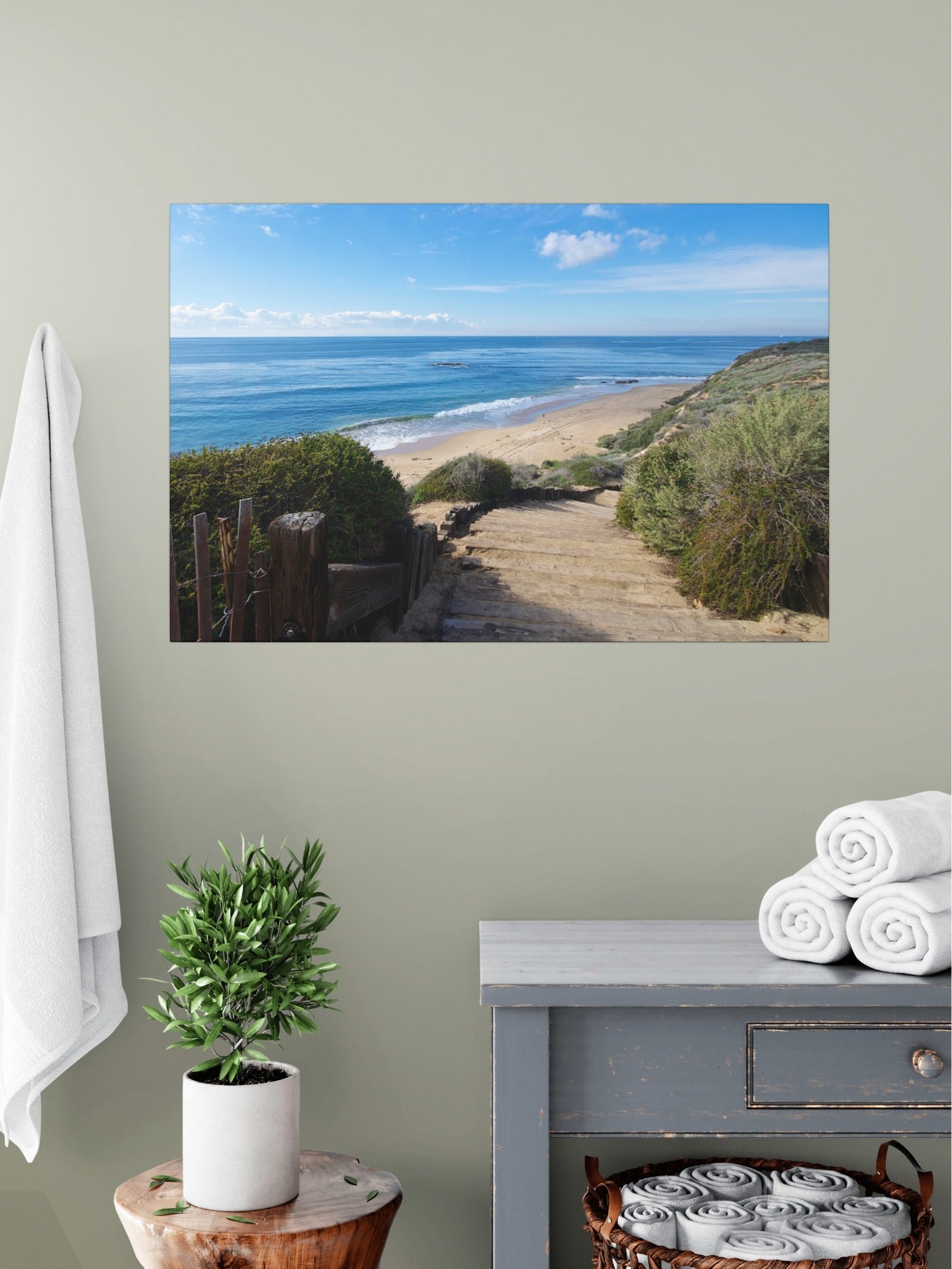 Canvas print of the wooden stairs leading to Crystal Cove State Beach in Orange County California on a wall above a table with a plant and folded towels.