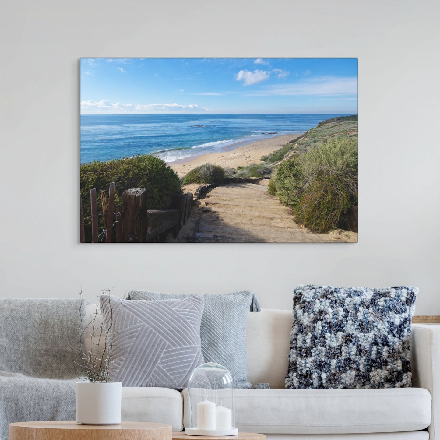 Canvas print of the wooden stairs leading to Crystal Cove State Beach in Orange County California hanging on a wall above a sofa with decorative pillows.