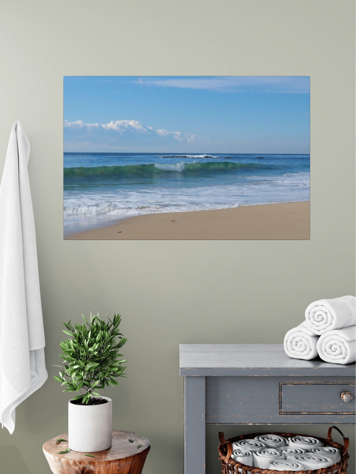 Crystal Cove State Beach breaking wave with translucent green water canvas print on a wall above a table with a plant and folded towels.