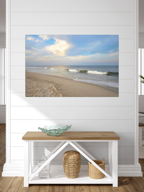 Canvas print of a wide-angle view of the Jersey Shore beach at early evening with rolling ocean waves and a bright, cloudy skyon a wall above a wooden bench with storage baskets.