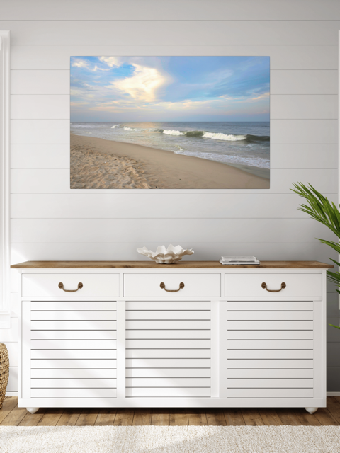 White cabinet with wooden top below a canvas print of a wide-angle view of the Jersey Shore beach at early evening with rolling ocean waves and a bright, cloudy sky.