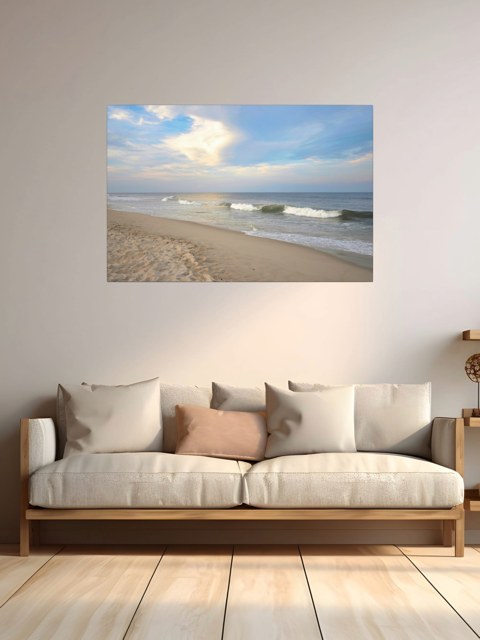 Canvas print of a wide-angle view of the Jersey Shore beach at early evening with rolling ocean waves and a bright, cloudy sky above a sofa in a room with wooden floor.