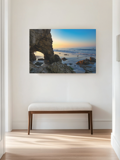 Canvas print of a sea cave at sunrise in Malibu on a wall in a room with a bench.
