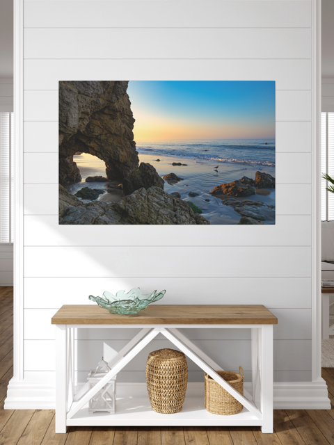 Canvas print of a sea cave at sunrise in Malibu on a white wall above a wooden bench.