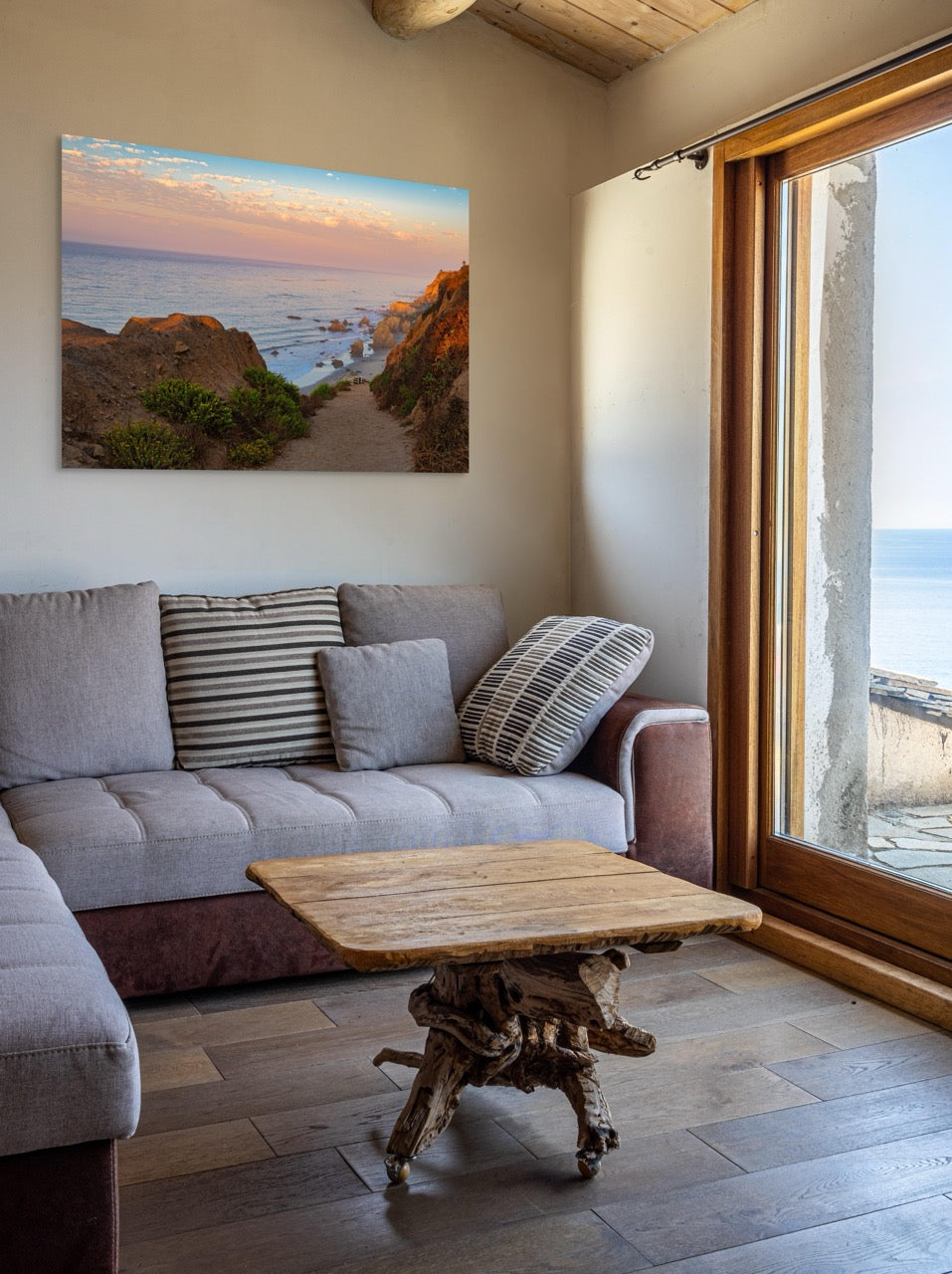 Living room with a gray sofa, wooden coffee table, and a large canvas print of a coastal landscape.