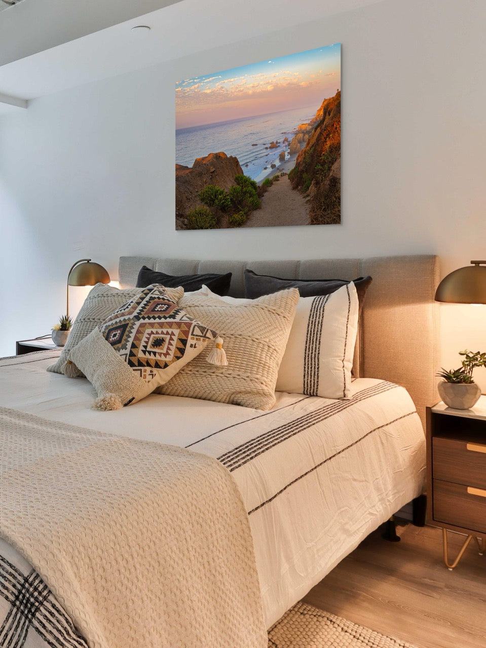 Bedroom with a bed featuring patterned pillows, a nightstand, and a large wall art of a coastal scene.