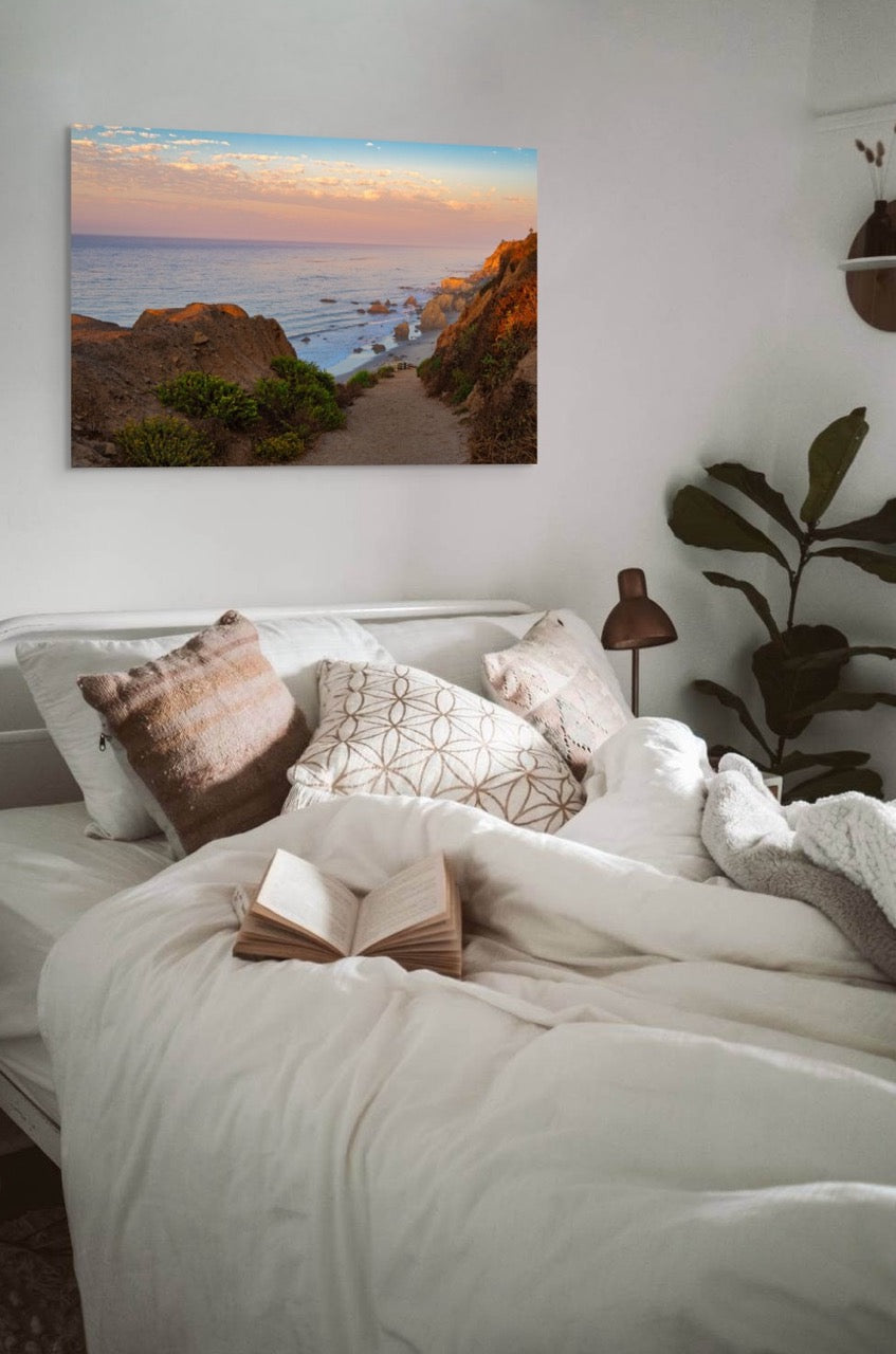 Bedroom with a large bed, decorative pillows, and a scenic wall art of a beach.