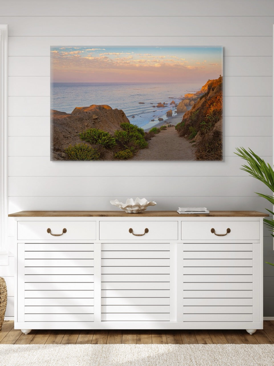 White cabinet with wooden top against a wall with a canvas print of a coastal landscape.