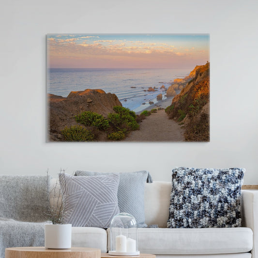 Canvas print of a coastal landscape above a living room sofa with decorative pillows.