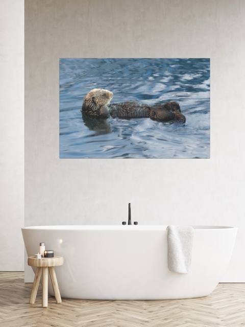 A sea otter canvas print on a wall above a white bathtub.