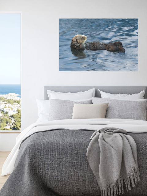 Sea otter canvas print  on a wall above a bed with gray bedding.