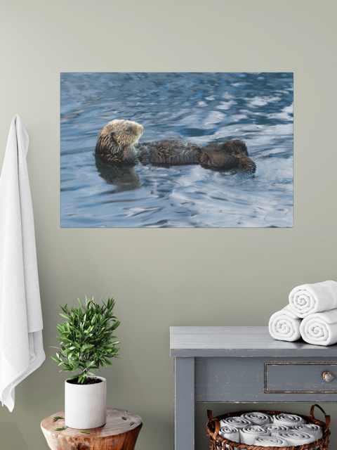 A sea otter canvas print above a gray cabinet with towels and a plant.