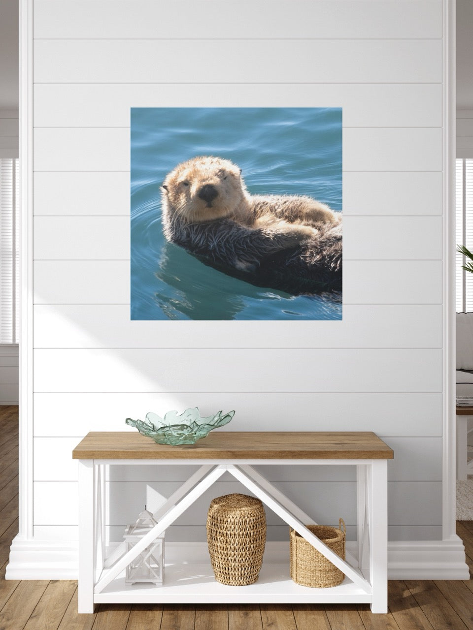 Canvas print of a sea otter in water on a white wall above a wooden bench with storage baskets.