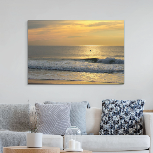Canvas print of a bird in flight over the ocean at sunrise on a wall above a sofa with decorative pillows.