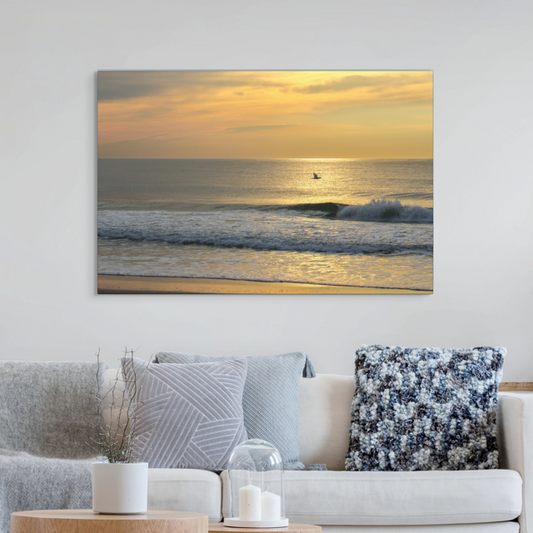 Canvas print of a bird in flight over the ocean at sunrise on a wall above a sofa with decorative pillows.