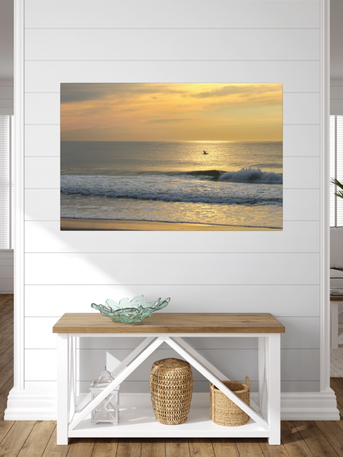Canvas print of a bird in flight over the ocean at sunrise on a wall above a wooden bench with storage.
