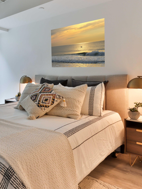 Bedroom with a bed featuring decorative pillows and a canvas print of a bird in flight over the ocean at sunrise on the wall.