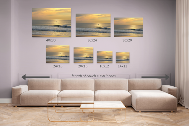 Seven different sized versions of a  canvas print of a bird in flight over the ocean at sunrise displayed above a sofa.