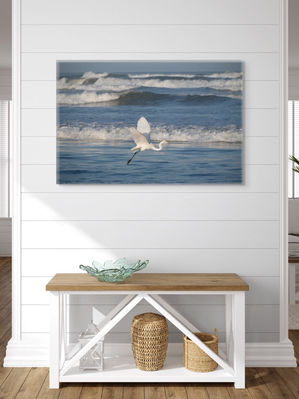Framed artwork of a white egret in flight over the ocean on a wall above a wooden bench.