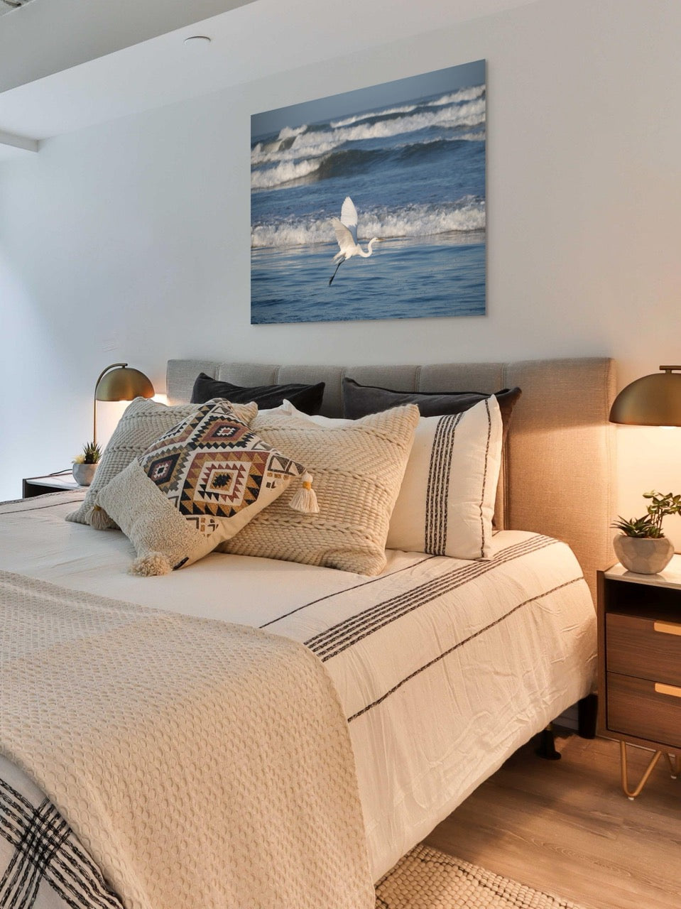 Bedroom with a bed featuring patterned pillows, a large canvas print of a white egret in flight over the ocean on the wall, and nightstands with lamps.