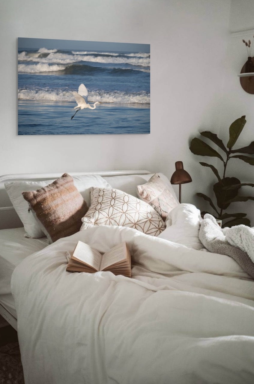 Bedroom with a large bed, decorative pillows, and a canvas print of a white egret in flight over the ocean on the wall.