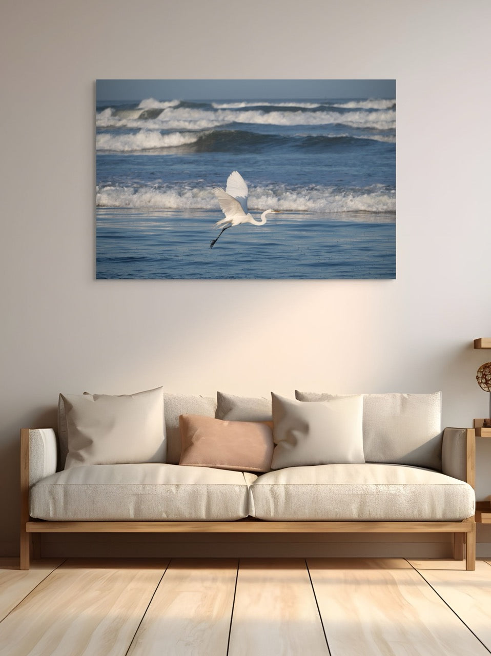 Beige sofa with decorative pillows in a room with a large canvas print of a white egret in flight over the ocean.