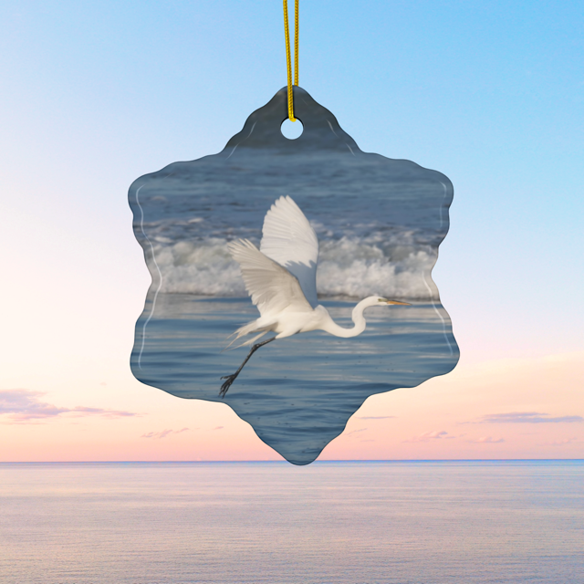 Ceramic Christmas ornament featuring a photograph of a white egret in flight over blue ocean waves with misty sea spray