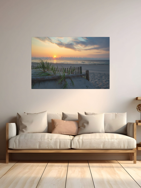 A canvas print featuring a sunrise over the ocean as seen from behind the dunes on the Jersey Shore above a sofa with cushions