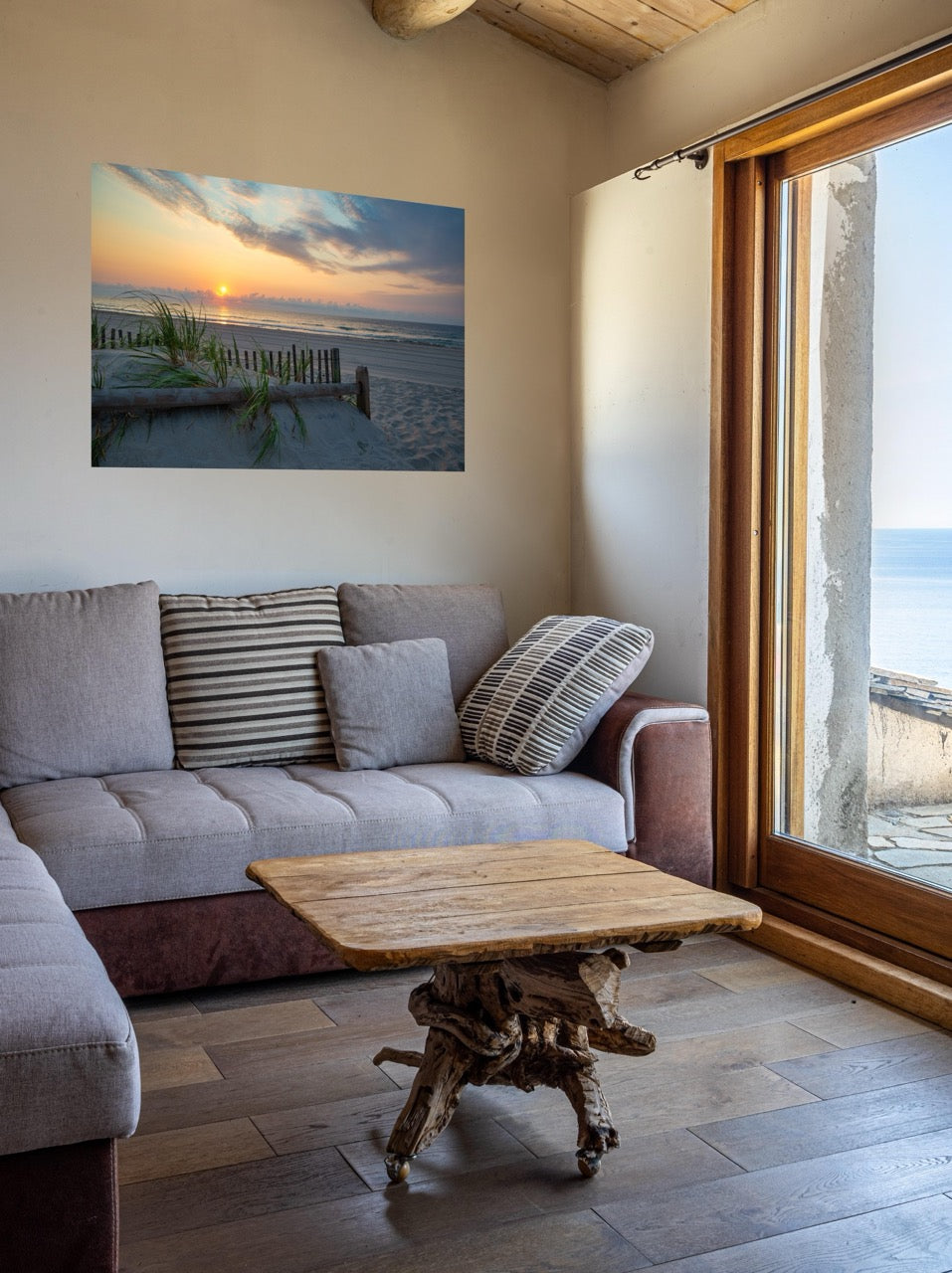 Living room with a gray sofa, wooden coffee table, and a canvas print featuring a sunrise over the ocean as seen from behind the dunes on the Jersey Shore on the wall.